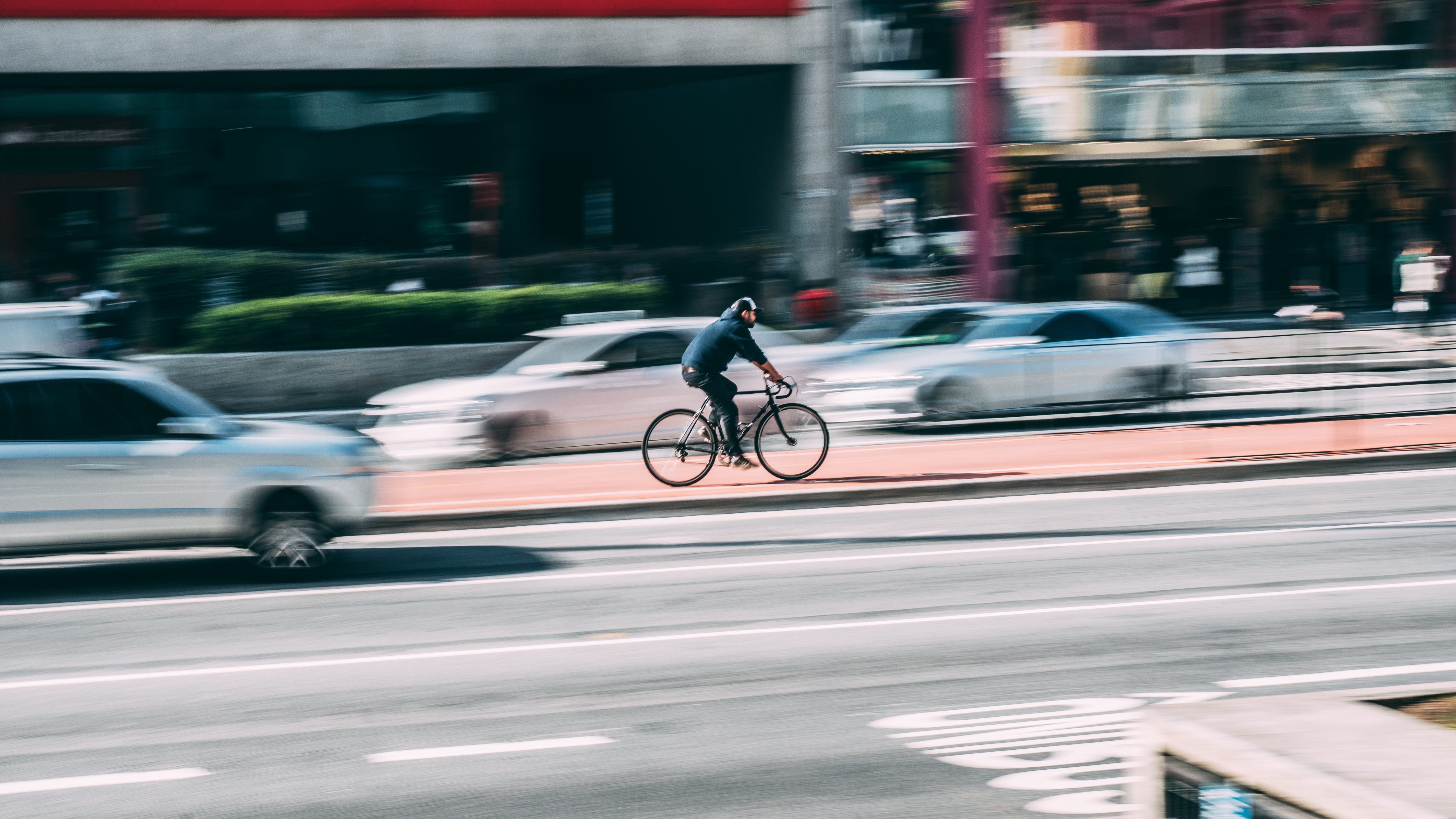 Cyklist bland bilar som kör snabbt i storstad.